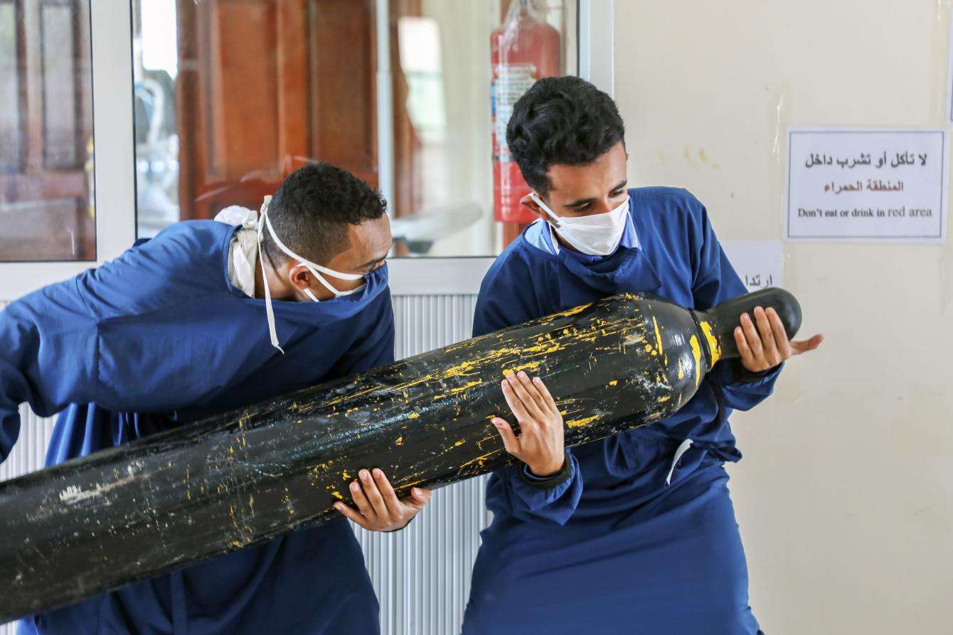 Workers carry an oxygen cylinder to the intensive care unit.