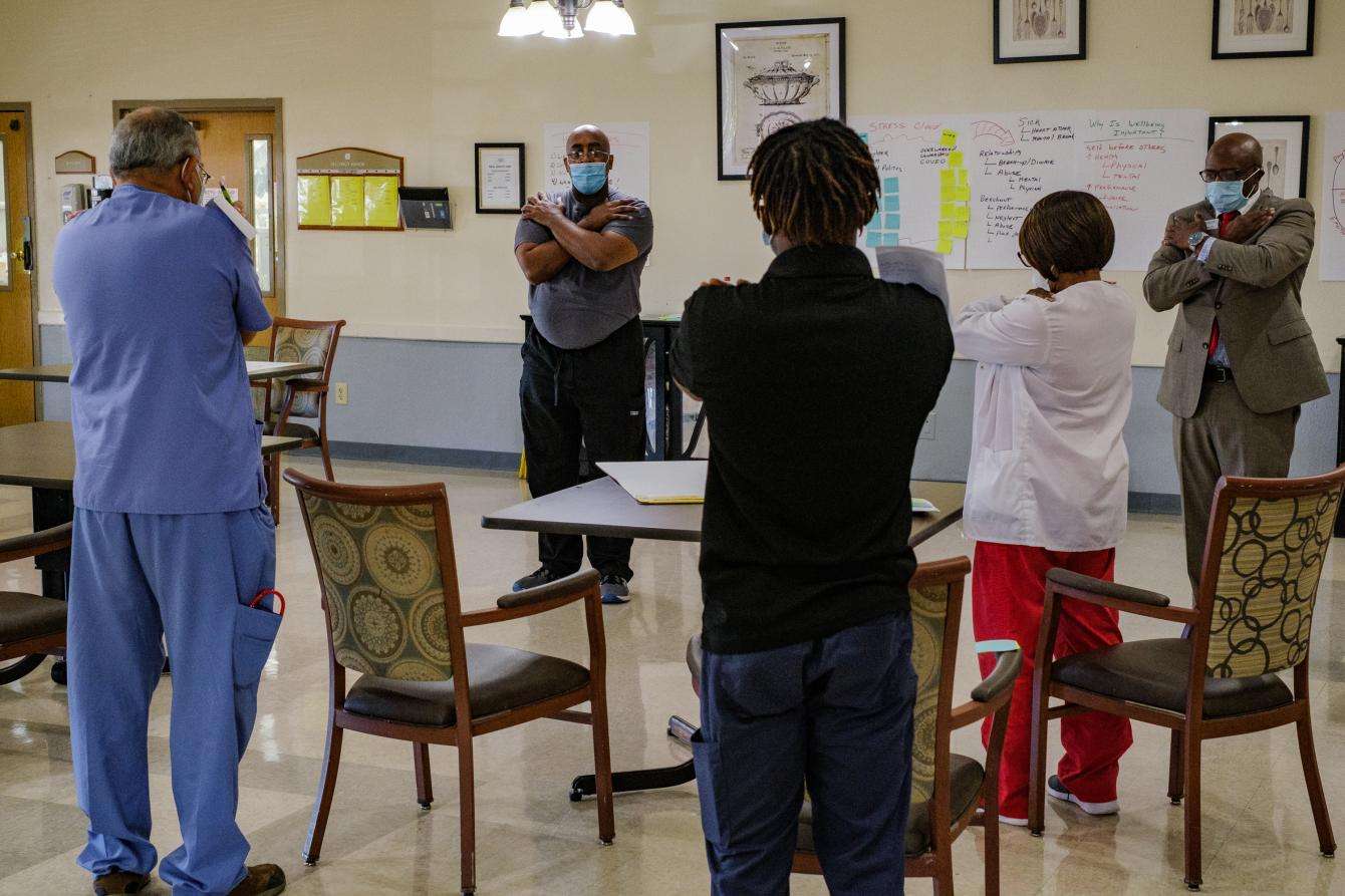 A group of nursing home staff stand together in a circle self-embracing.