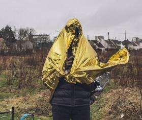 A young migrant covers himself with a survival blanket on a rainy day in Calais.