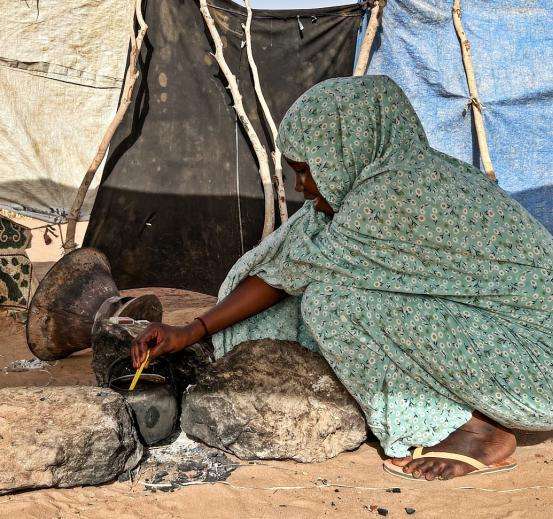 A Sudanese refugee woman crouching over a fire pit in Chad.